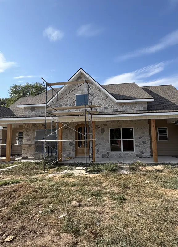 Stone and siding ranch home with scaffolding during exterior finish